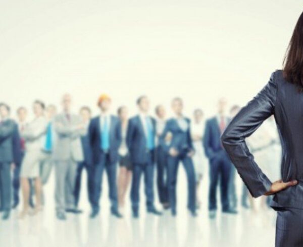 A confident businesswoman stands with her back to a group of professionals.
