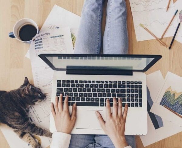 Person typing on a laptop with coffee and documents nearby.